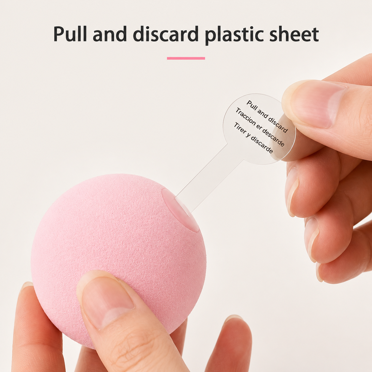 A hand holds a pink ball while another hand pulls a clear plastic strip attached to it, with text at the top reading 'Pull and discard plastic sheet.'.