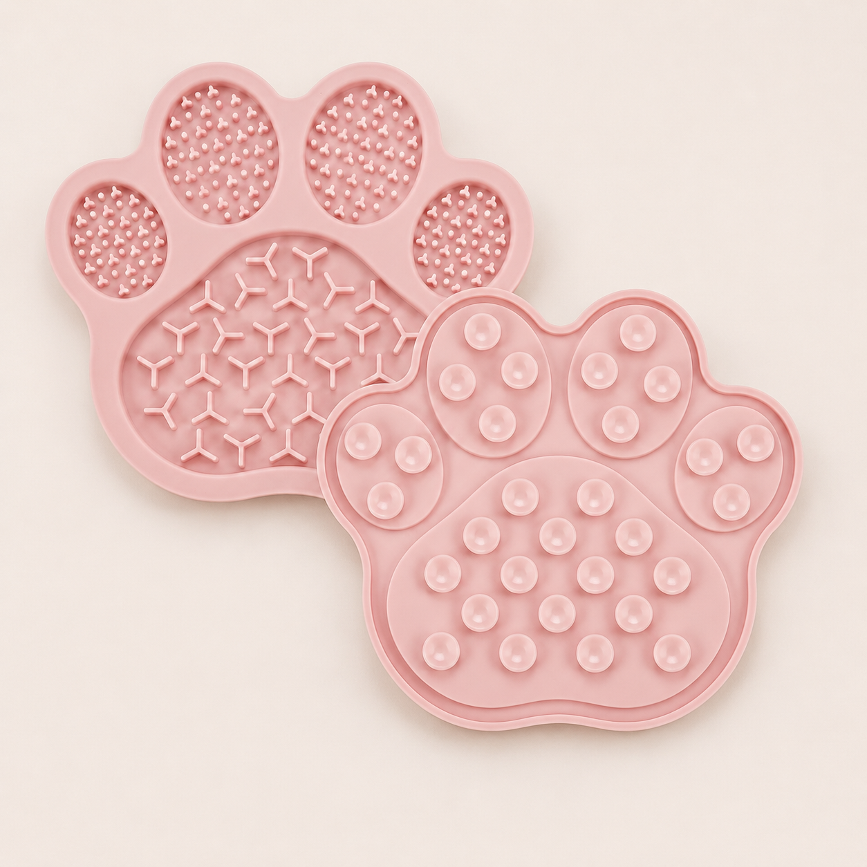 Two pink paw-shaped silicone pet slow feeding mats showing textured elements on one side and suction cups on the other, shown on a light cream background.