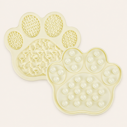 Two pale yellow paw-shaped silicone slow feeding mats with textured and raised circular patterns, shown on a light cream background.