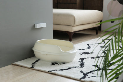 White pet litter box on a patterned rug with a smart odour eliminator mounted to the wall above it with a couch in the background