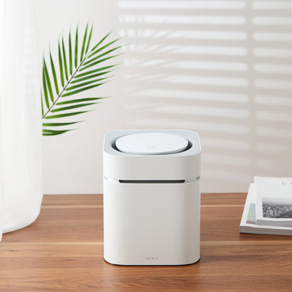 White air purifier on a wooden table with a plant and books in the background