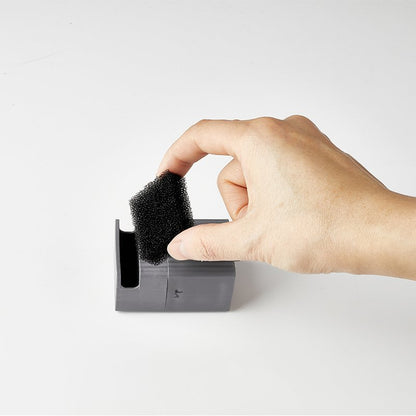 Hand holding a black replacement filter over a grey holder on a white background