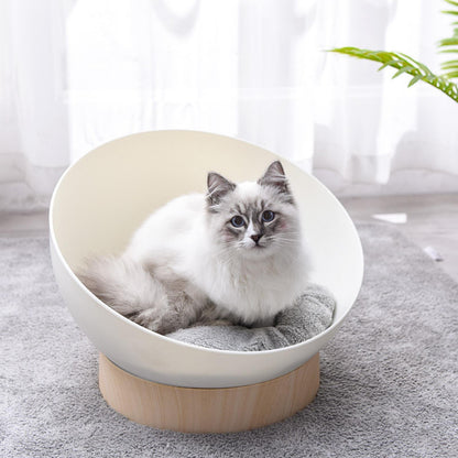 Cat lying in a white pet bed with wooden base on a light gray carpet.
