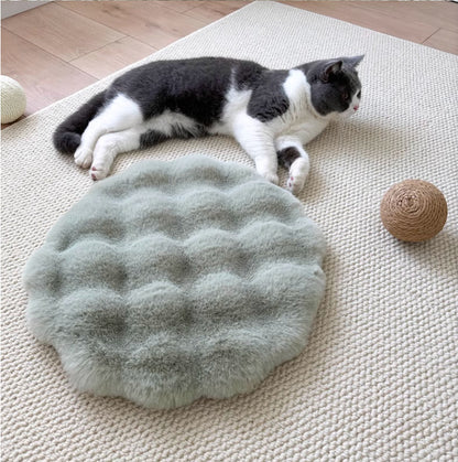Cat lying on a textured green grey rug mat with a round ball of yarn