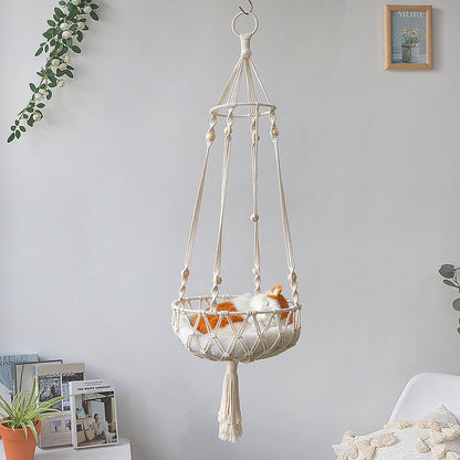 Macrame hanging pet bed with tassels hanging against a light gray wall.