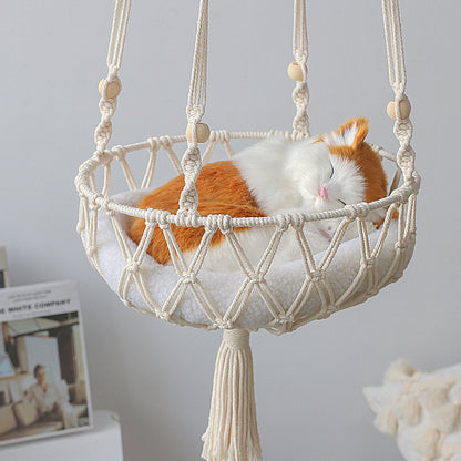 Cat lying in a macrame pet hammock against a neutral background