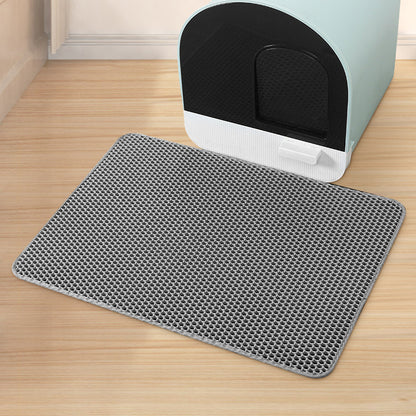 Gray litter mat with black hexagonal pattern in front of a cat litter box on a wooden floor.