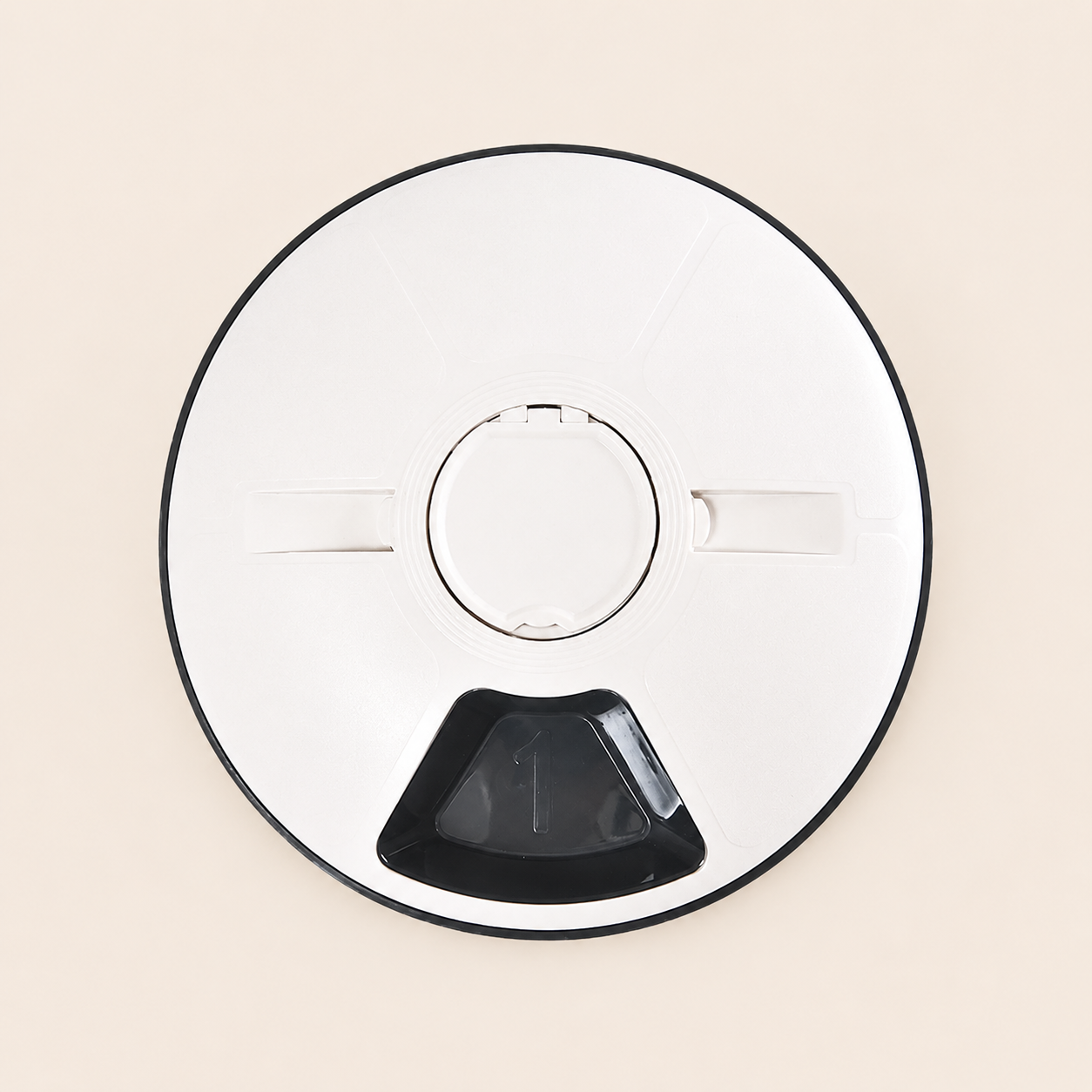 A top-down view of a circular automatic pet feeder with a black rim, a central circular opening, two small side tabs, and a black triangular opening at the bottom, set against a solid light beige background.